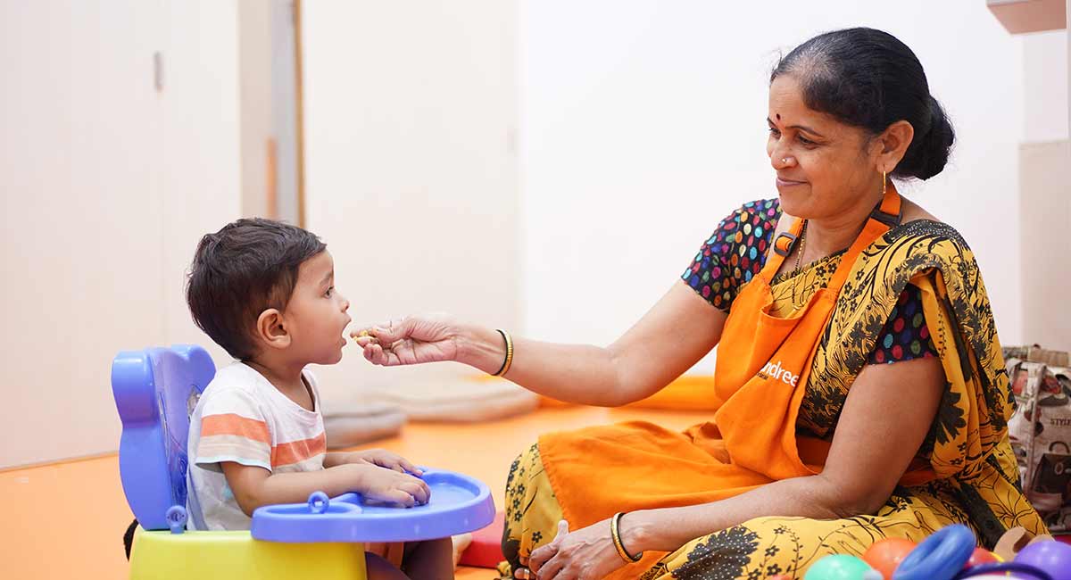 Teacher feeding toddler nutritious meal at preschool